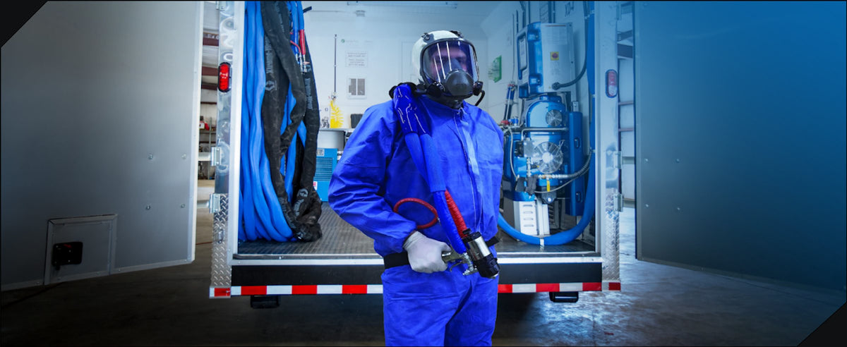ArmorThane applicator in protective suit with spray gun in front of a mobile spray rig